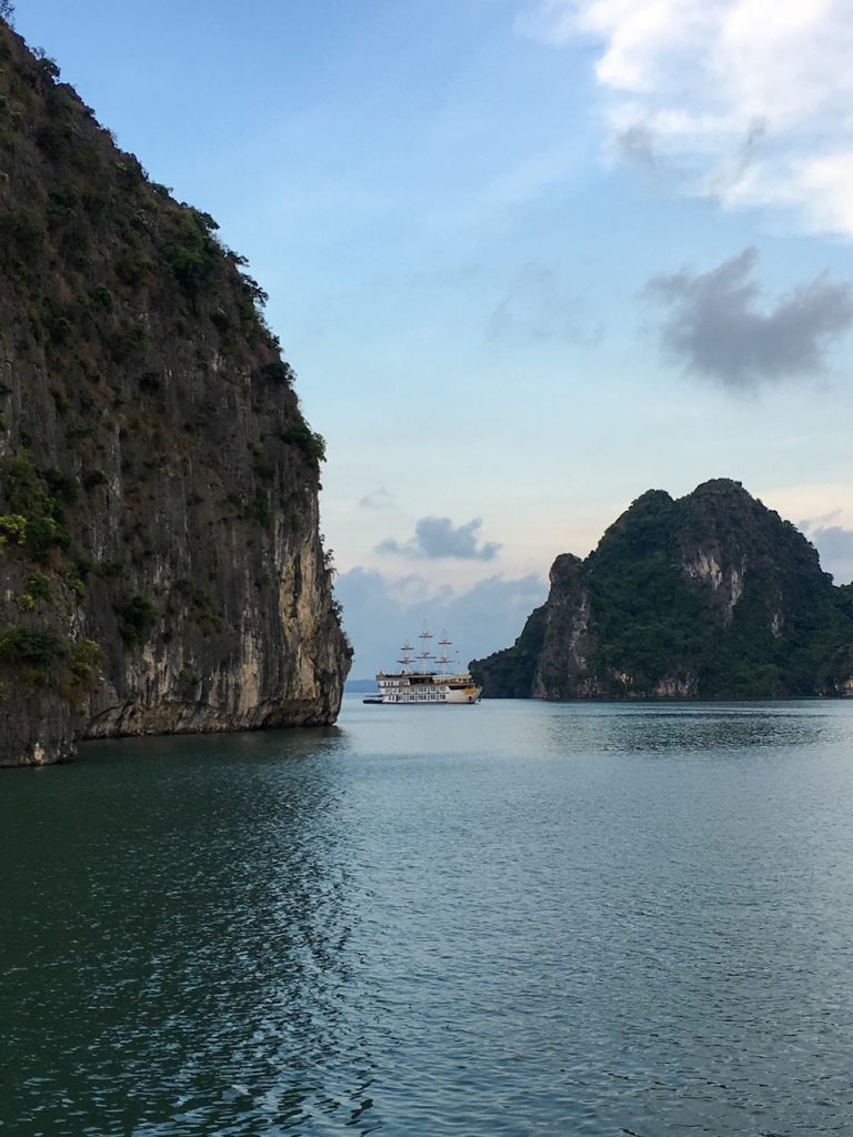 a boat floating through the limestone karsts at Bai Tu Long Bay