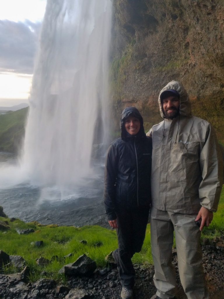 Sara and Tim wearing their wet weather gear from this hiking packing list and standing in front of Seljalandsfoss, a waterfall you can walk behind in Iceland