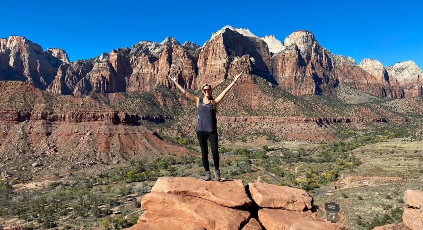Sara posing on top of a rock at Watchman Overlook with Zion Canyon in the background on the Watchman Trail in Zion