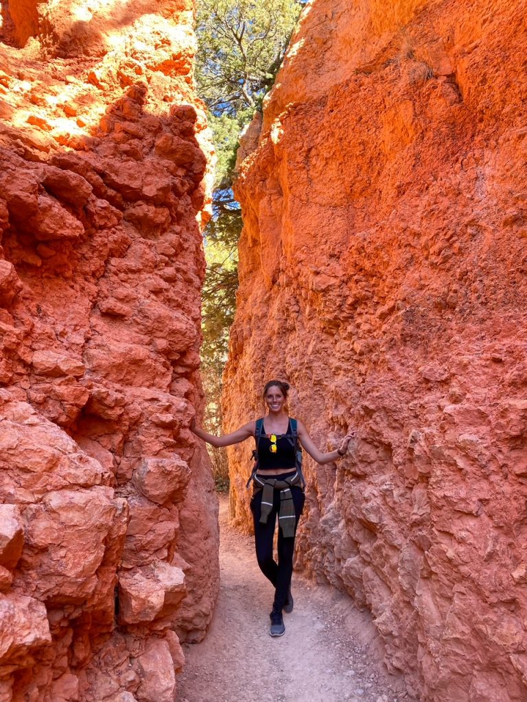 Sara walking through bright orange canyon walls formed by hoodoos in Bryce Canyon National Park