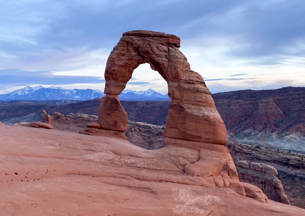 Delicate Arch glowing at sunset with the La Sal Mountains in the background, the most famous landmark in Arches National Park on a Mighty Five trip