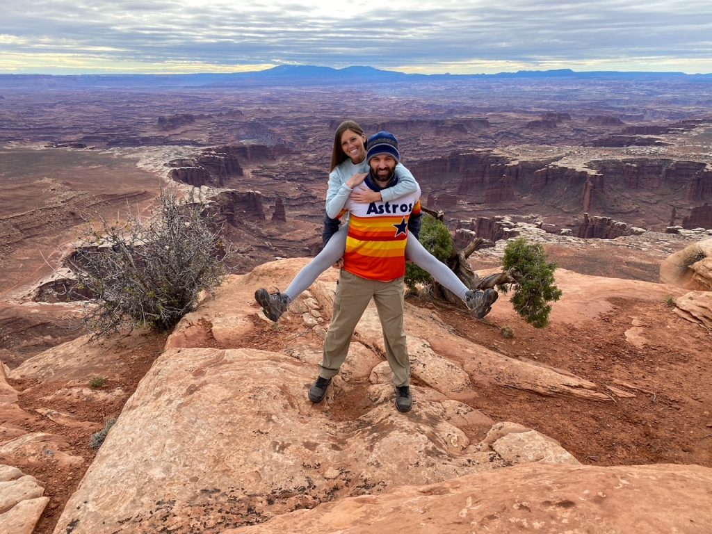 Sara on Tim's back in front of Monument Basin in Canyonlands National Park, one of the least visited of the Utah national parks