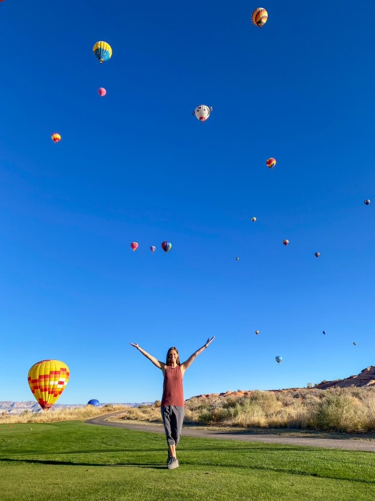Sara with her hands up in front of a bunch of hot air balloons in flight at the Lake Powell Balloon Regatta in Page, AZ