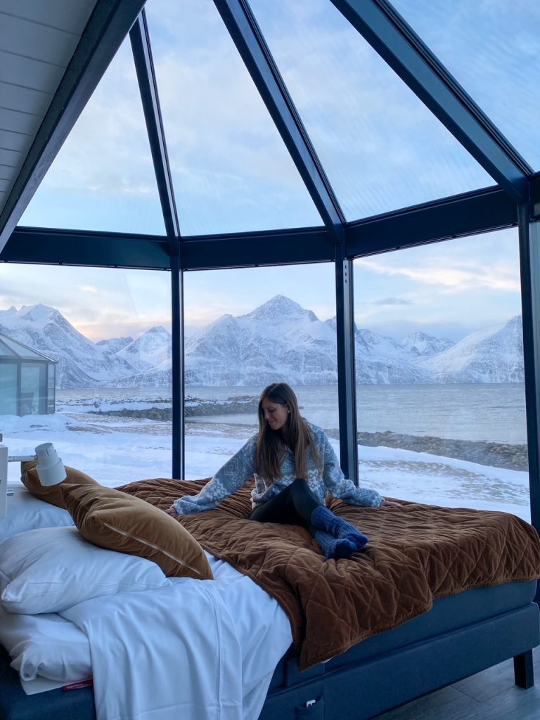 Sara sitting on the bed in the 180 degree glass igloo at Lyngen North Igloo Hotel