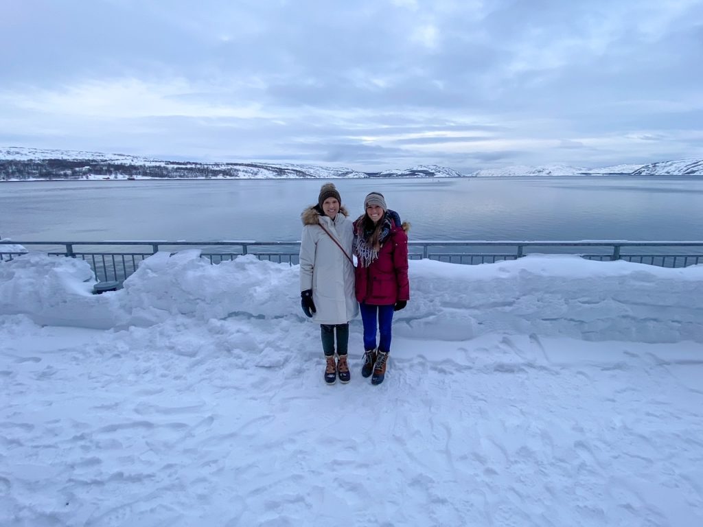 two girls in all their winter gear standing in front of the Bøkfjorden in Kirkenes, Norway