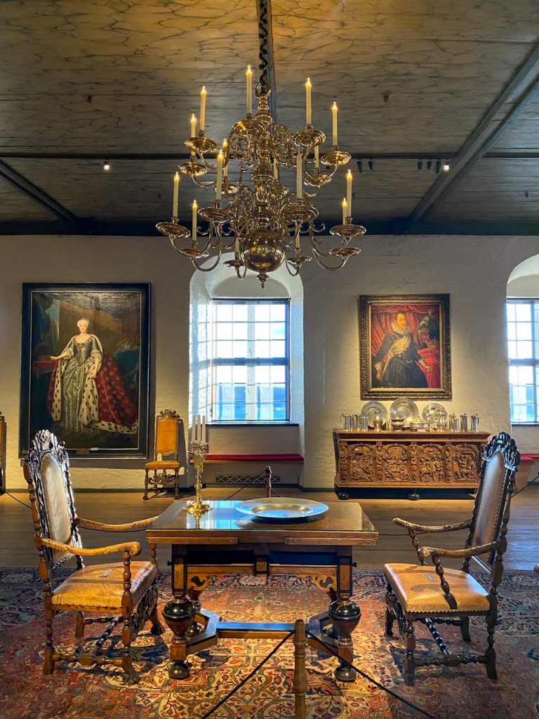 a royal table set for two with a gold chandelier above and two portraits in the background inside Akershus Fortress in Oslo