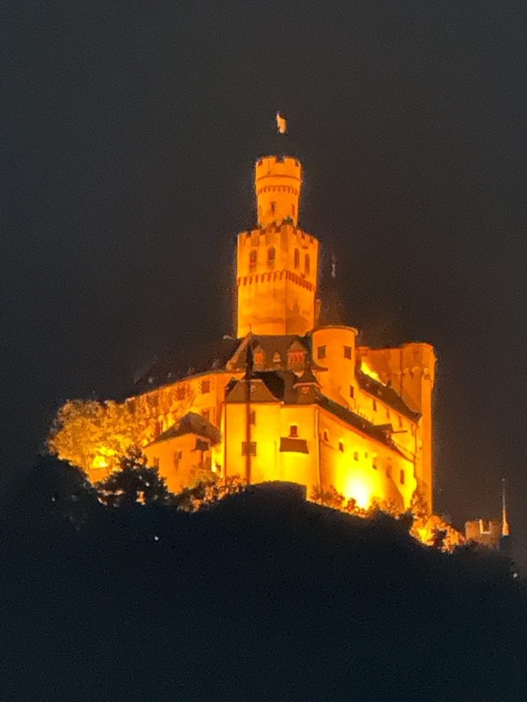 Marksburg Castle lit up at night from the Braubach train platform