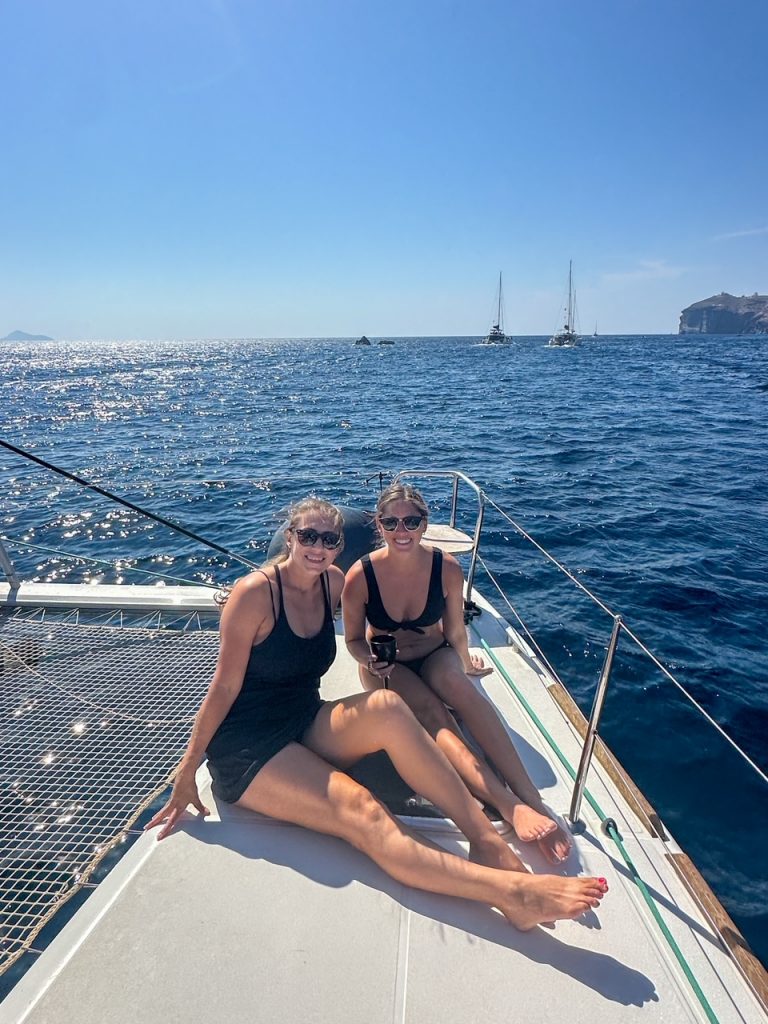 Kristen & Sara sitting on the side of the catamaran in Santorini