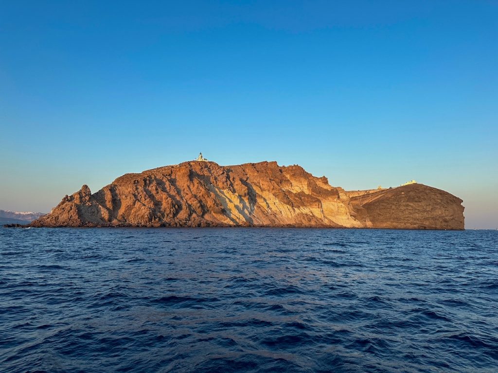 a pretty island view with a historic Venetian lighthouse as seen from our Santorini catamaran cruise