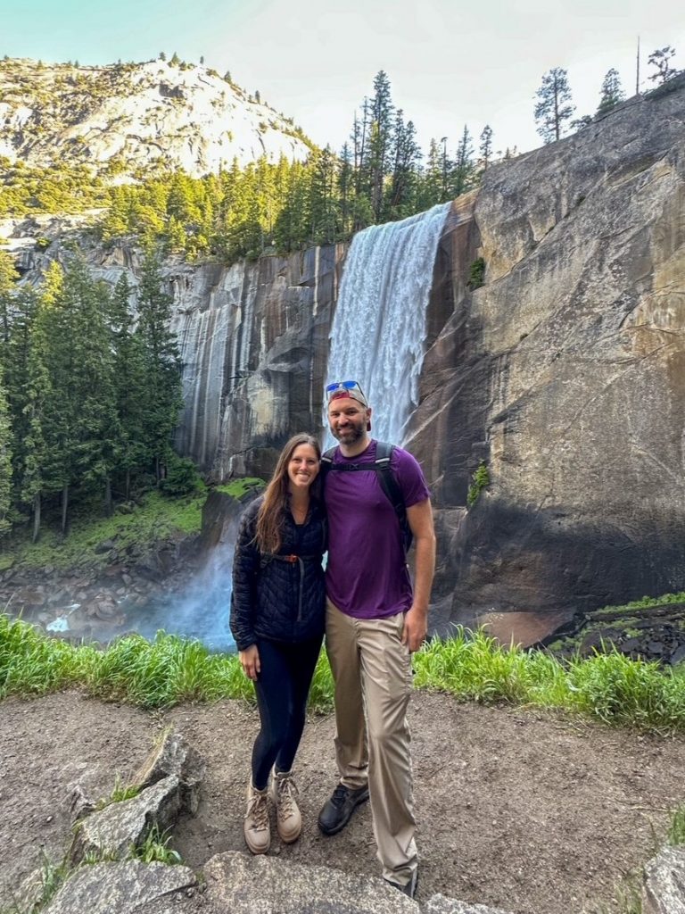 Sara and Tim with all of their hiking gear standing in front of Vernal Fall in Yosemite National Park