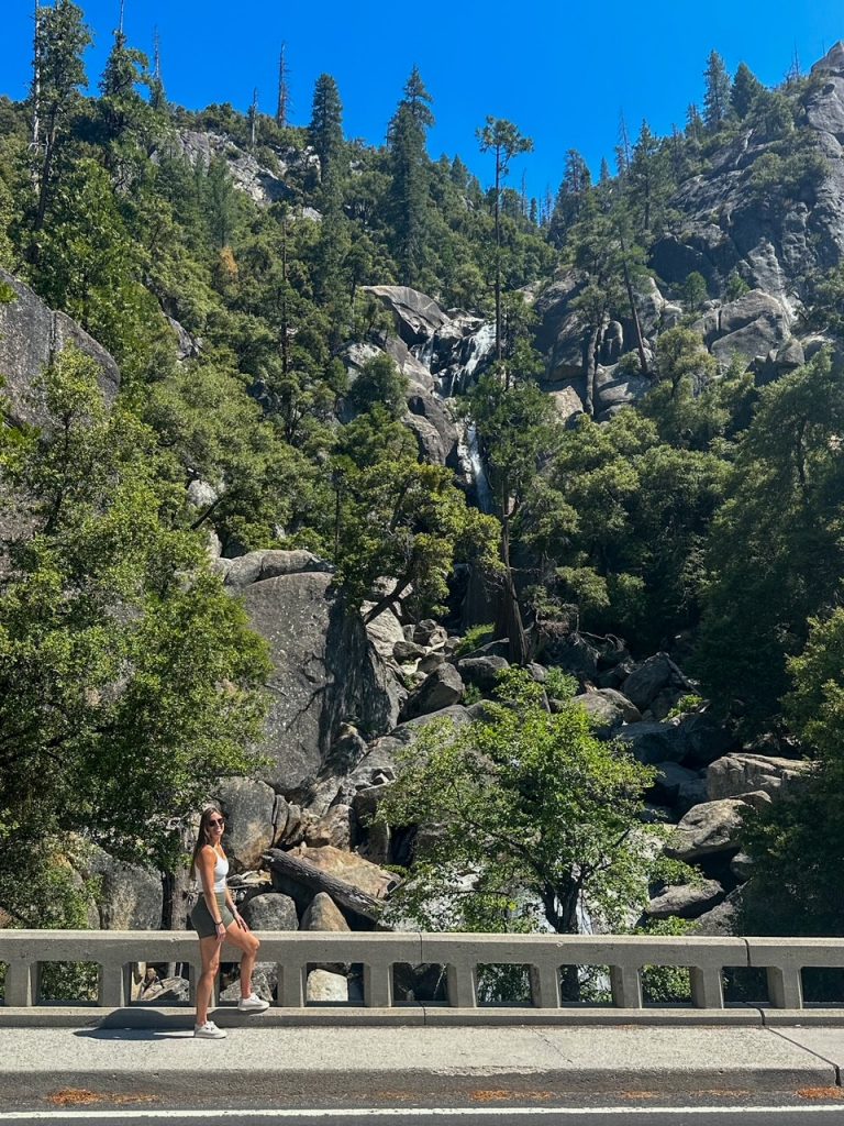Sara in front of a waterfall on the side of the road in Yosemite National Park