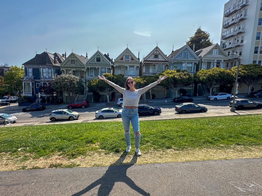Traveler posing in front of the Painted Ladies in San Francisco with the downtown skyline in the background