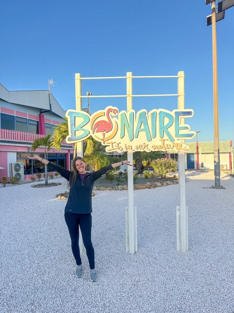 Sara with the Bonaire welcome sign at Flamingo Airport